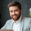 Professional smiling man in a suit sitting at a laptop, representing excellent communication and customer service in tree care.